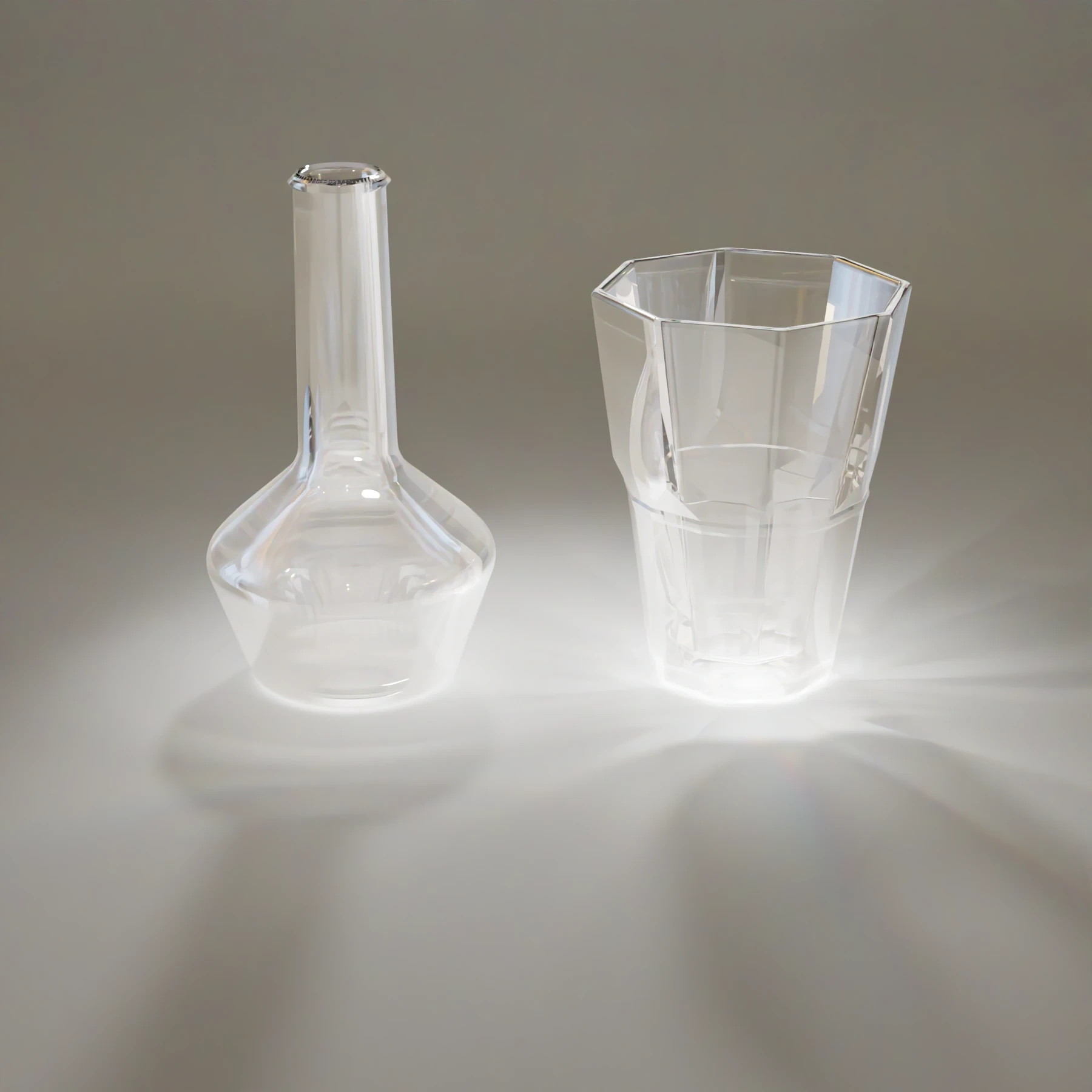A long-necked flask and a faceted glass, both clear, on a light grey surface with strong brightness and soft shadows around their bases.